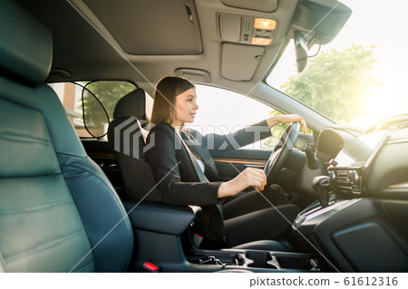 Driving around city. Young attractive business woman in black suit smiling and looking straight while driving a car Driving around city. Young attractive business woman in black suit smiling and looking straight while driving a car 61612316