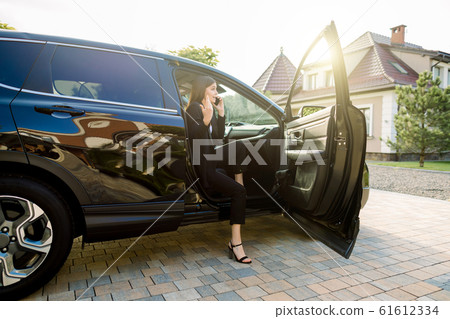 Beautiful emotional business woman is talking on the mobile phone, while sitting on the passenger seat in the car with open door Beautiful emotional business woman is talking on the mobile phone, while sitting on the passenger seat in the car with open door 61612334