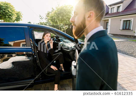 Young beautiful business woman getting out the front door in her car. Driver or business partner helping woman to get outside the car Young beautiful business woman getting out the front door in her car. Driver or business partner helping woman to get outside the car 61612335
