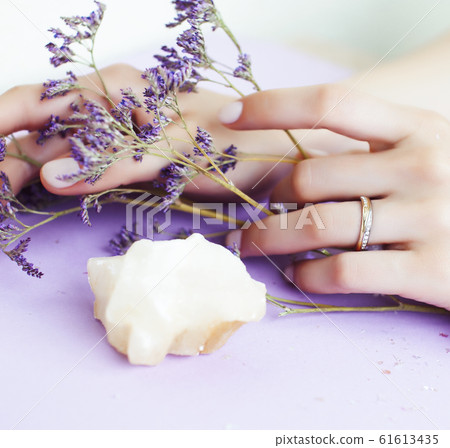 pretty perfect woman hands with white manicure and little flowers on colorful lilac background, green leaf spa concept 61613435