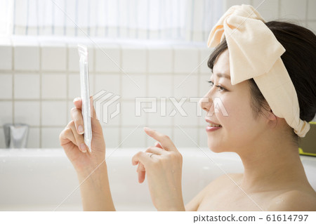 通過將智能手機放在浴室的防水盒中看智能手機的年輕女子 通過將智能手機放在浴室的防水盒中看智能手機的年輕女子 61614797