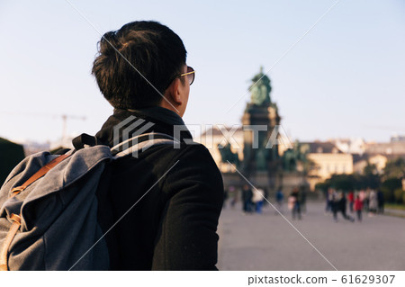 Back view portrait of Asian male tourist backpacker carrying a bag in Maria Theresa Monument in Vienna, Austria 61629307