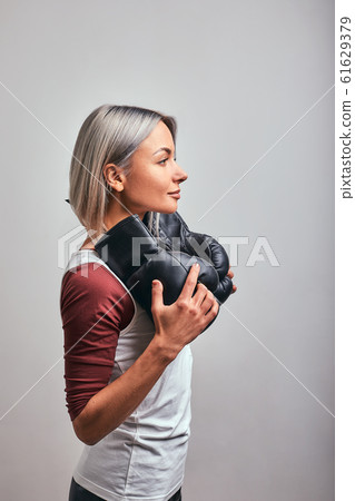 Young beautiful sexy woman boxer posing with black boxing gloves in her hands on a gray background. Copy space, gray background, goal achievement. 61629379