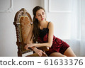 Beautiful young woman sitting on a vintage armchair in red pajama set 61633376