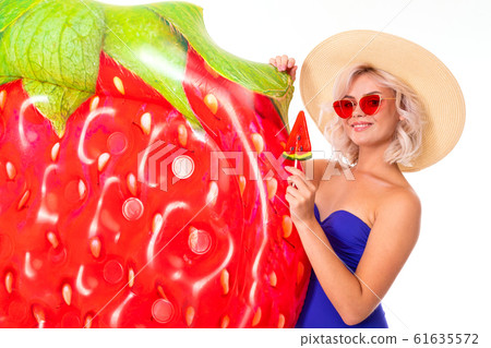 Pretty blonde caucasian female stands in swimsuit with rubber beach mattress, drinks juice and Pretty blonde caucasian female stands in swimsuit with rubber beach mattress, drinks juice and 61635572