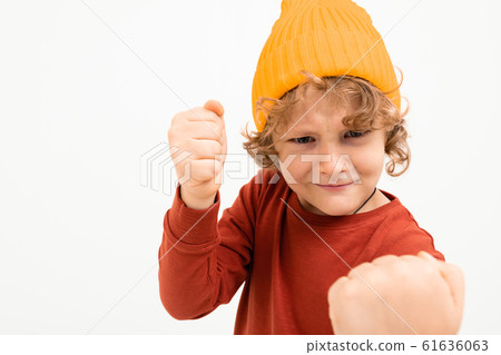 Portrait of charming boy with curly hair, yellow hat shows fists isolated on white background 61636063