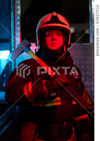 Close up firefighter male with hammer on his shoulder standing near fire engine 61637512