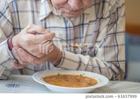 Elderly man with Parkinsons disease holds spoon in 61637999
