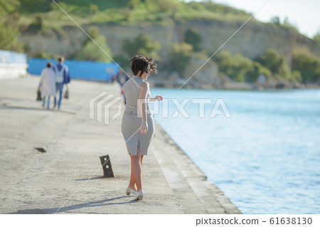 A woman walks along a concrete embankment along the sea A woman walks along a concrete embankment along the sea 61638130