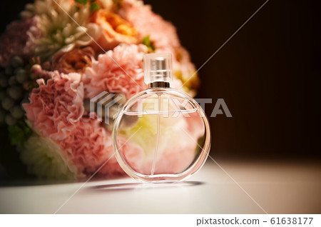 A round bottle of perfume on a dark background, near a bouquet with pink flowers.Aromatherapy and perfumes. 61638177