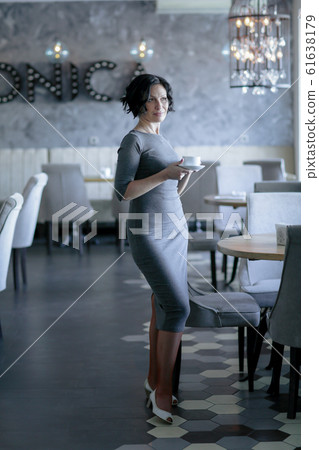 A beautiful successful adult woman stands in a cafe and drinks coffee from a Cup 61638179