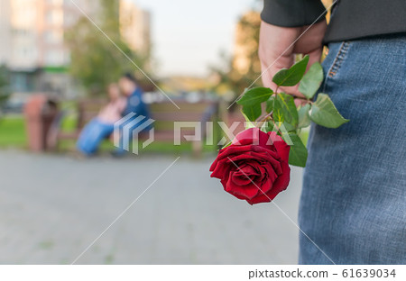 view of a man with a rose flower on the background of a couple sitting on a bench in the Park view of a man with a rose flower on the background of a couple sitting on a bench in the Park 61639034