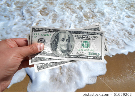 Girl holding a money bill of 300 dollars on background of sea waves Girl holding a money bill of 300 dollars on background of sea waves 61639262