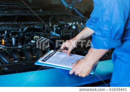 Car mechanic holding clipboard and checking to 61639401