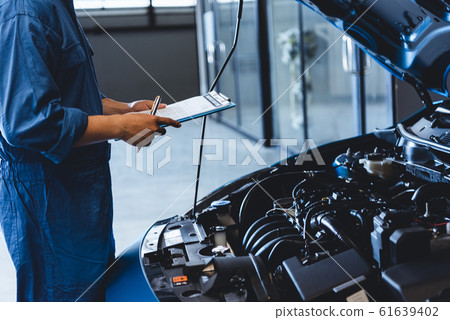 Car mechanic holding clipboard and checking to 61639402