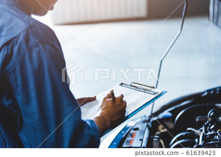 Car mechanic holding clipboard and checking to 61639423