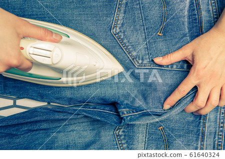 Image on top of man ironing blue jeans on ironing board Image on top of man ironing blue jeans on ironing board 61640324
