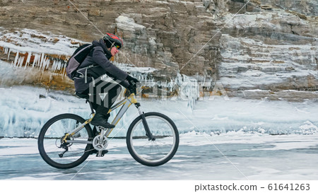 Man is riding bicycle near ice grotto. Rock with ice caves icicl Man is riding bicycle near ice grotto. Rock with ice caves icicl 61641263