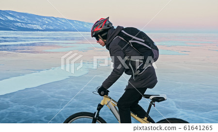 Man is riding bicycle on the ice. Ice of frozen Lake Baikal. Tee Man is riding bicycle on the ice. Ice of frozen Lake Baikal. Tee 61641265