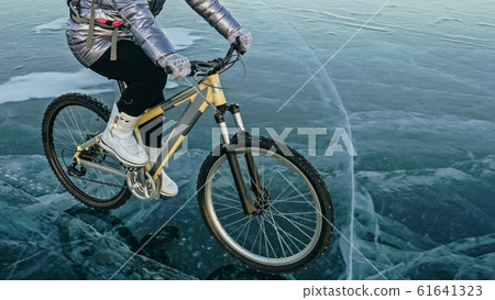 Woman is riding bicycle on the ice. Tires on bike are covered wi 61641323