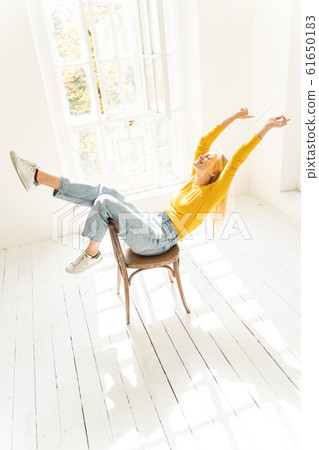 Relaxed young lady in yellow sweater sitting on chair near the window 61650183
