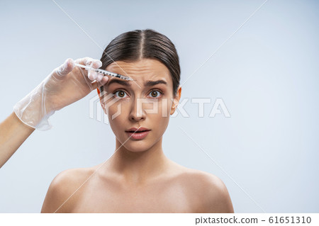 Scared young girl is posing for camera against light background Scared young girl is posing for camera against light background 61651310