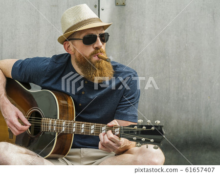 Man with fedora and cigar playing acoustic guitar 61657407