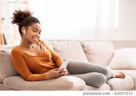 Afro Woman Listening To Music On Smartphone Sitting On Sofa Afro Woman Listening To Music On Smartphone Sitting On Sofa 61657515