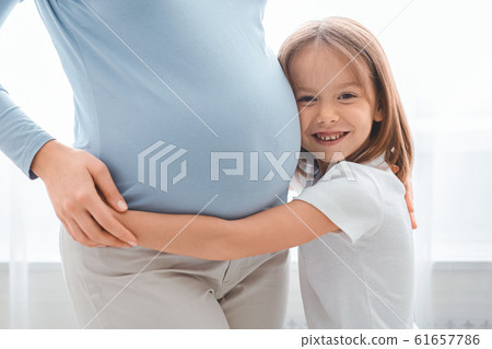 Excited little girl embracing her pregnant mother tummy 61657786