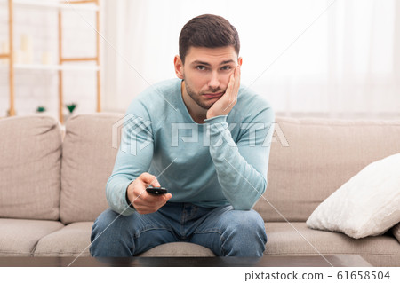 Bored Guy Switching Channels Watching TV Sitting On Couch Indoor Bored Guy Switching Channels Watching TV Sitting On Couch Indoor 61658504