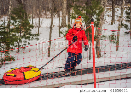 Boy with tubing rises on a travelator to the mountain. Child having fun on snow tube. Boy is riding 61659631