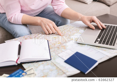 Senior woman choosing trip on map, booking hotel on laptop 61662327
