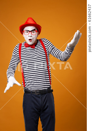 Young mime looking at camera in vest and red hat Isolated on orange background 61662437