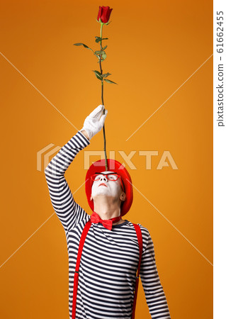 Mime in vest and red hat looking up with rose on his forehead isolated 61662455