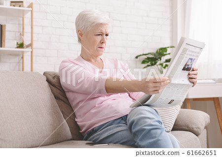 Senior lady squinting and holding newspaper far from eyes Senior lady squinting and holding newspaper far from eyes 61662651