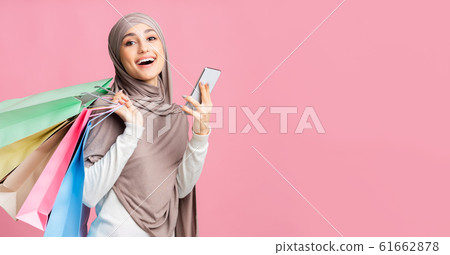 Happy islamic woman in hijab holding smartphone and paper shopping bags 61662878