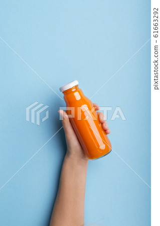 A bottle of orange juice or detox drink in a woman's hand over blue A bottle of orange juice or detox drink in a woman's hand over blue 61663292