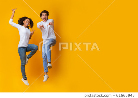 Funny Interracial Couple Jumping In Air On Yellow Background In Studio 61663943