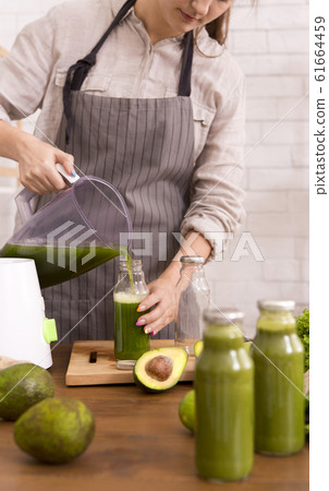 Young woman on detox diet pouring green cocktail from mixer 61664459
