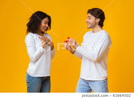 Romantic guy proposing to his surprised girlfriend, giving ring Romantic guy proposing to his surprised girlfriend, giving ring 61664502