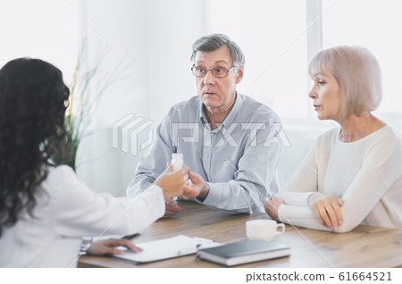 Nurse gives senior man plastic pill jar at office Nurse gives senior man plastic pill jar at office 61664521