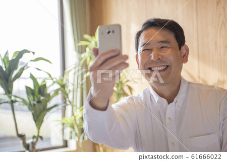 Middle-senior man taking a selfie with a smartphone in the living room 61666022