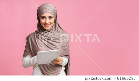 Millennial muslim girl in hijab with digital tablet over pink background Millennial muslim girl in hijab with digital tablet over pink background 61666253
