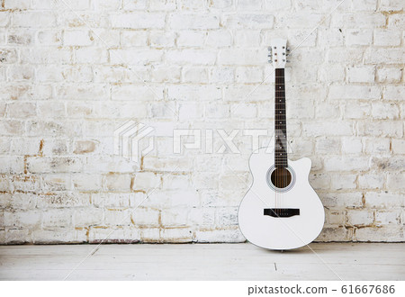 Acoustic white guitar leaning against a white wall 61667686