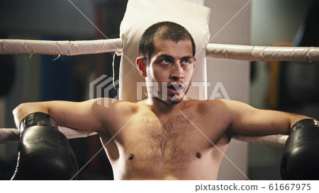 A man boxer sitting in the corner of the ring with a teeth guard in the mouth A man boxer sitting in the corner of the ring with a teeth guard in the mouth 61667975