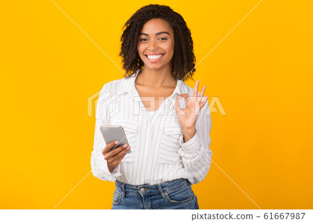 Portrait of smiling black woman using phone showing ok gesture Portrait of smiling black woman using phone showing ok gesture 61667987