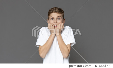 Scared teen boy biting nails in fear 61668168