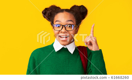 Afro teenager pointing up over yellow studio wall 61668260