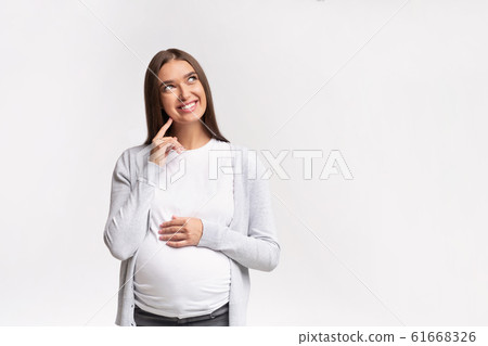 Cheerful Mother-To-Be Dreaming Standing Over White Background In Studio Cheerful Mother-To-Be Dreaming Standing Over White Background In Studio 61668326