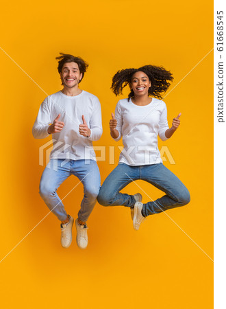 Joyful interracial couple jumping in the air and gesturing thumbs up 61668545